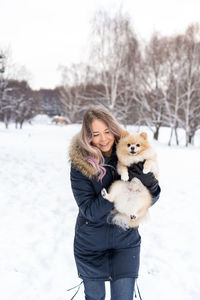 Young woman carrying dog while standing in snow during winter