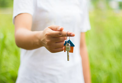 Midsection of man holding keychain while standing on grassy field