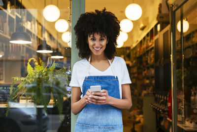 Portrait of smiling woman with cell phone standing in entrance door of a store