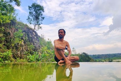 Full length of shirtless man standing by lake against sky