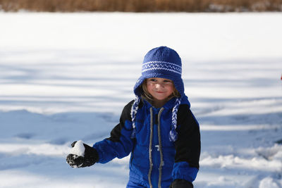 Little boy holding snowball outside in blue snowsuit