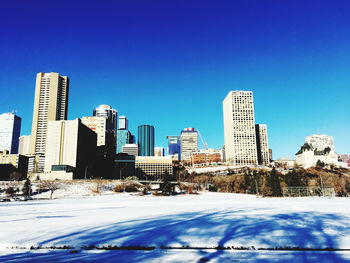 Snow covered buildings in city against blue sky