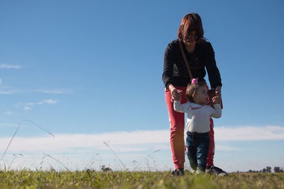 Rear view of mother and daughter on field against sky