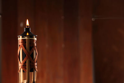 Close-up of illuminated tiki torch against wooden wall
