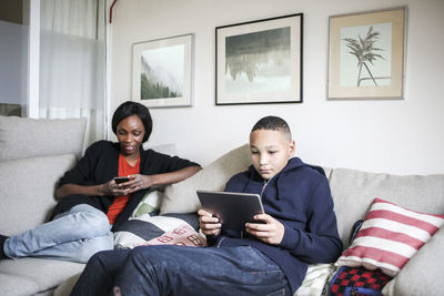 Mother and son using technologies on sofa at home