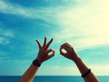 Cropped hands of person gesturing ok sign against sea and sky