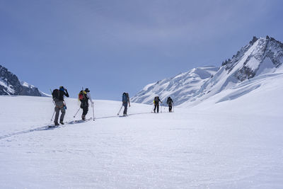 Full length of ski mountaineers walking on snowcapped mountain against sky