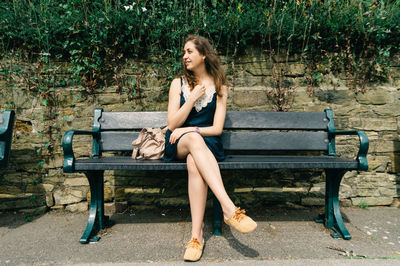 Young woman sitting on bench against retaining wall at park