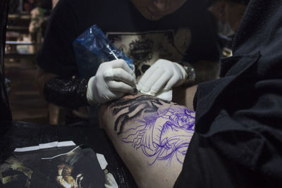 Artist tattooing on thigh of woman at studio