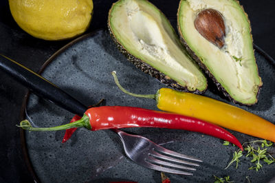 Black plate with sliced avocado and red and yellow peppers