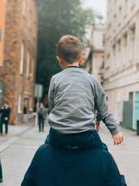 Rear view of man walking on street against buildings in city