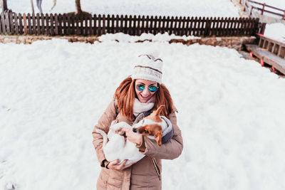 Cheerful woman carrying dog while standing on snowy land