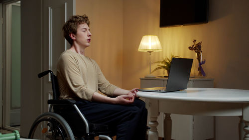 Young man meditating while sitting by laptop at home