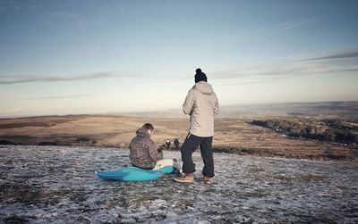 Rear view of man with friend sitting on sled against landscape
