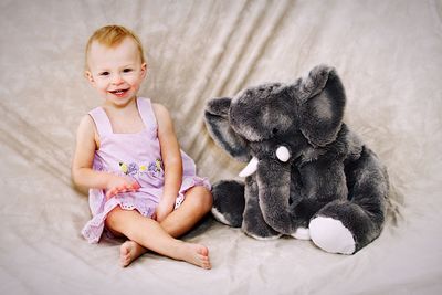 Portrait of cute smiling girl with stuffed toy sitting on bed at home