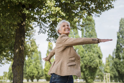 Happy senior woman with outstretched arms in a park