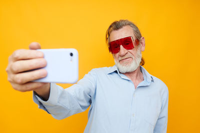 Senior man taking selfie against yellow background