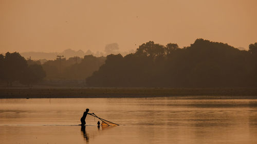 Silhouette man in lake against sky during sunset