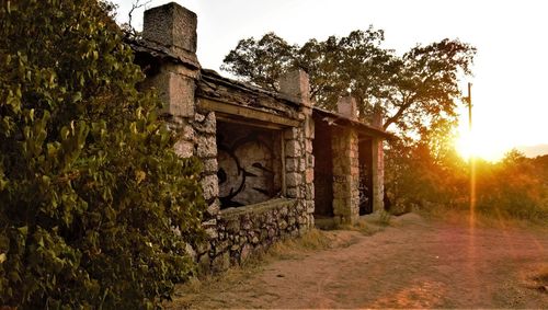 Old building by trees against sky during sunset