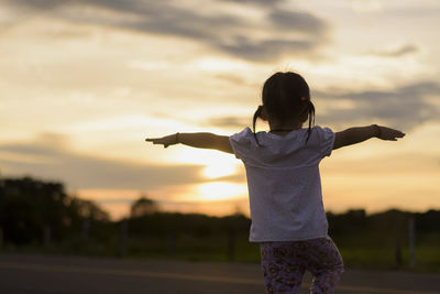 Rear view of woman standing against sky during sunset