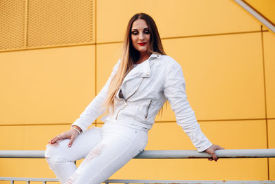 Beautiful woman sitting on railing against yellow wall