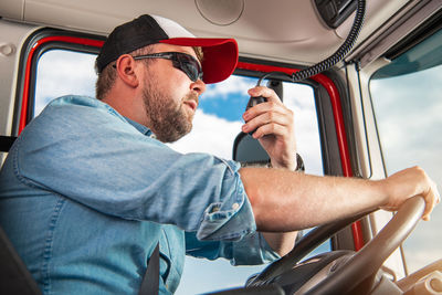 Caucasian semi truck driver in his 30s taking conversation using cb radio inside his truck cabin.