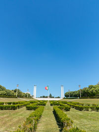 Road amidst field against clear blue sky