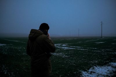 Rear view of man standing on field against clear sky