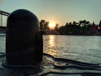 Close-up of metal by sea against sky during sunset