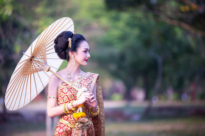 Beautiful woman in traditional clothing looking away while holding paper umbrella