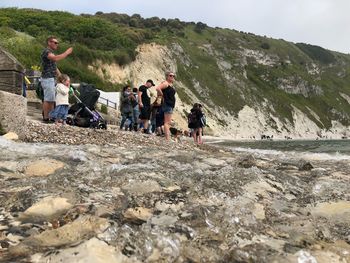 People on rocks by mountains against sky