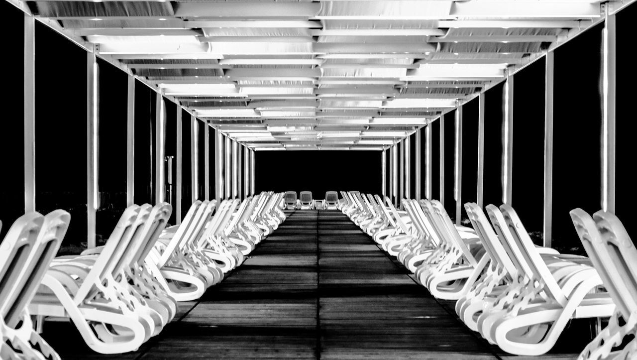 in a row, indoors, empty, the way forward, no people, direction, absence, architecture, illuminated, seat, repetition, diminishing perspective, lighting equipment, built structure, pattern, railing, large group of objects, wood - material, arrangement, chair