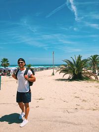 Portrait of male tourist standing at beach against blue sky