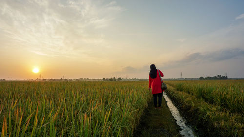 Rear view of woman standing on field against sky during sunset