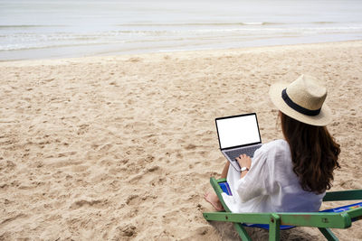 Rear view of woman using mobile phone at beach