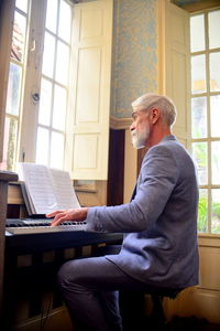 Side view of man in suit  playing the piano at home