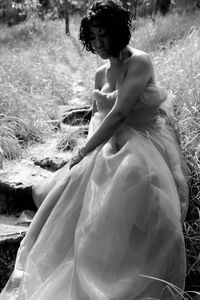 Female model wearing gown sitting on field in forest