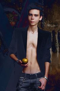 Portrait of man holding golden apple while standing against wall