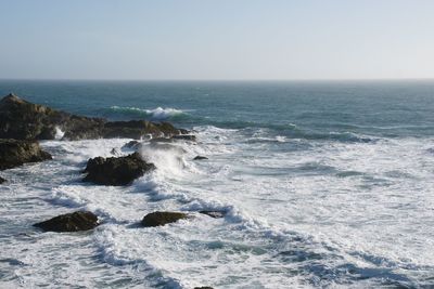 Scenic view of waves against clear sky during sunny day