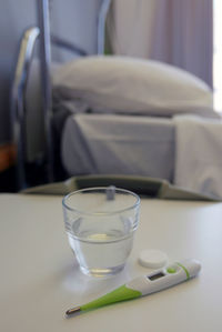 Pill and water glass with thermometer on table in hospital