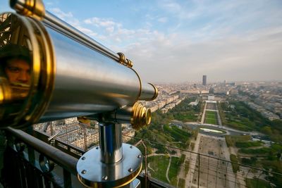 Reflection of man on telescope against cityscape and sky