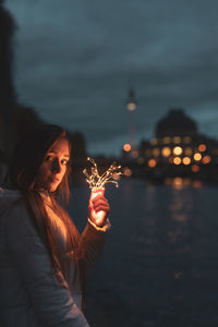 Portrait of young woman holding illuminated string light at night