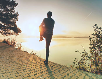 Rear view of man walking on footpath against sky during sunset