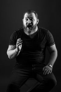 Portrait of man sitting against black background