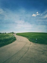 Country road amidst a field against the blue sky