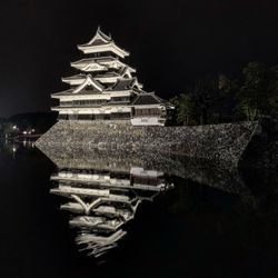 Illuminated building by lake against sky at night