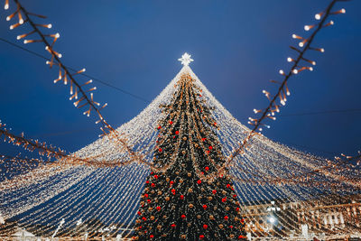 Christmas tree with red toy balls, star and golden lights in the festive evening city bokeh garlands