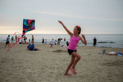 Full length of girl flying kite at beach during sunset