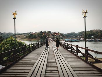 Rear view of people on bridge over river against sky