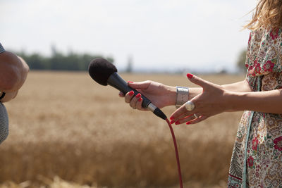 Midsection of woman holding microphone on field